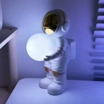 Lámpara astronauta blanco sosteniendo esfera luminosa, con visor dorado, ideal para ambientación.