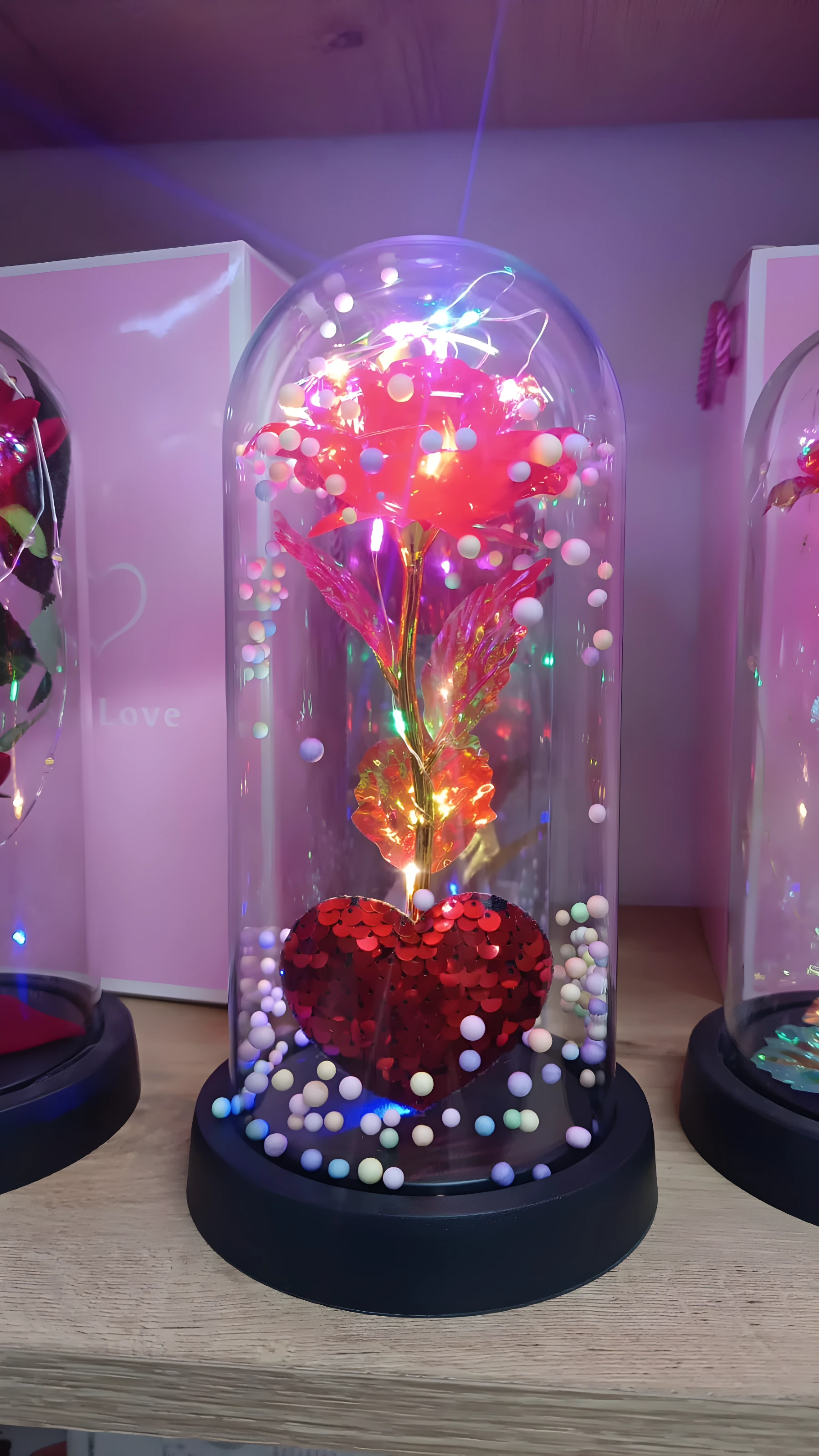 Rosa roja brillante en cúpula de cristal con luces LED y base de corazón de lentejuelas.
