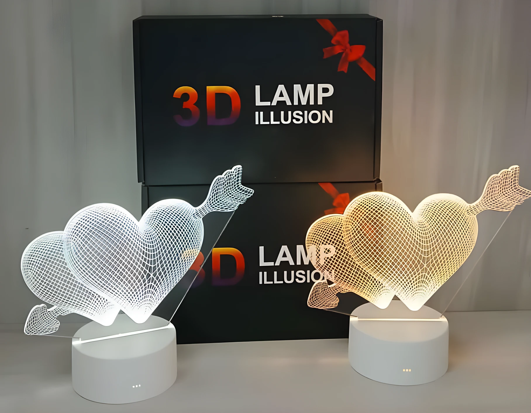 Lámparas 3D de corazón flechado, una blanca y otra amarilla, sobre bases circulares blancas, frente a cajas de regalo.