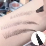 Demostración de plumín de cejas y barba marrón oscuro con punta de microcuchillas dibujando trazos de vello sobre piel clara.