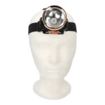 Linterna LED frontal minera con aro reflectante cobre, montada sobre cabeza maniquí blanca, con dos botones de control naranjas.