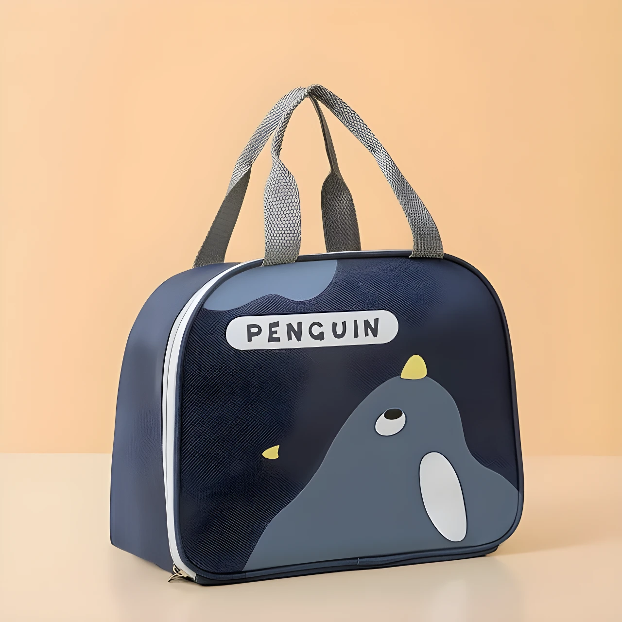 Lonchera térmica azul marino con diseño de pingüino, asas grises, cremallera blanca. Ideal para mantener alimentos frescos.