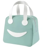 Lonchera térmica portátil color verde menta con diseño de cara sonriente, asas blancas y cierre de cremallera lateral para transporte de alimentos.
