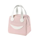Lonchera térmica portátil color rosa con diseño de carita sonriente, fabricada en material liso, cuenta con cierre de cremallera y asas blancas.