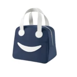 Lonchera térmica portátil azul marino con diseño de cara sonriente blanca, cremallera lateral y asas superiores reforzadas para transporte práctico.