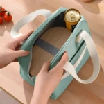 Lonchera térmica color verde menta con asas blancas, manos abriendo el compartimento principal que contiene un recipiente de madera y una lata de bebida.
