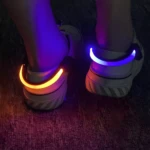 Taloneras deportivas LED. Par de luces de seguridad flexibles, una naranja y una azul, sujetas a tenis blancos en la oscuridad.