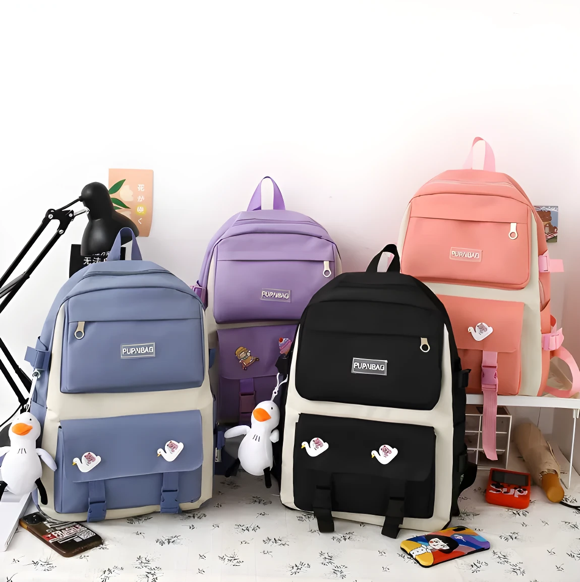 Cuatro bolsos tipo maleta de diferentes colores (morado, azul, negro, rosa) con diseños juveniles y detalles de patos y cisnes.