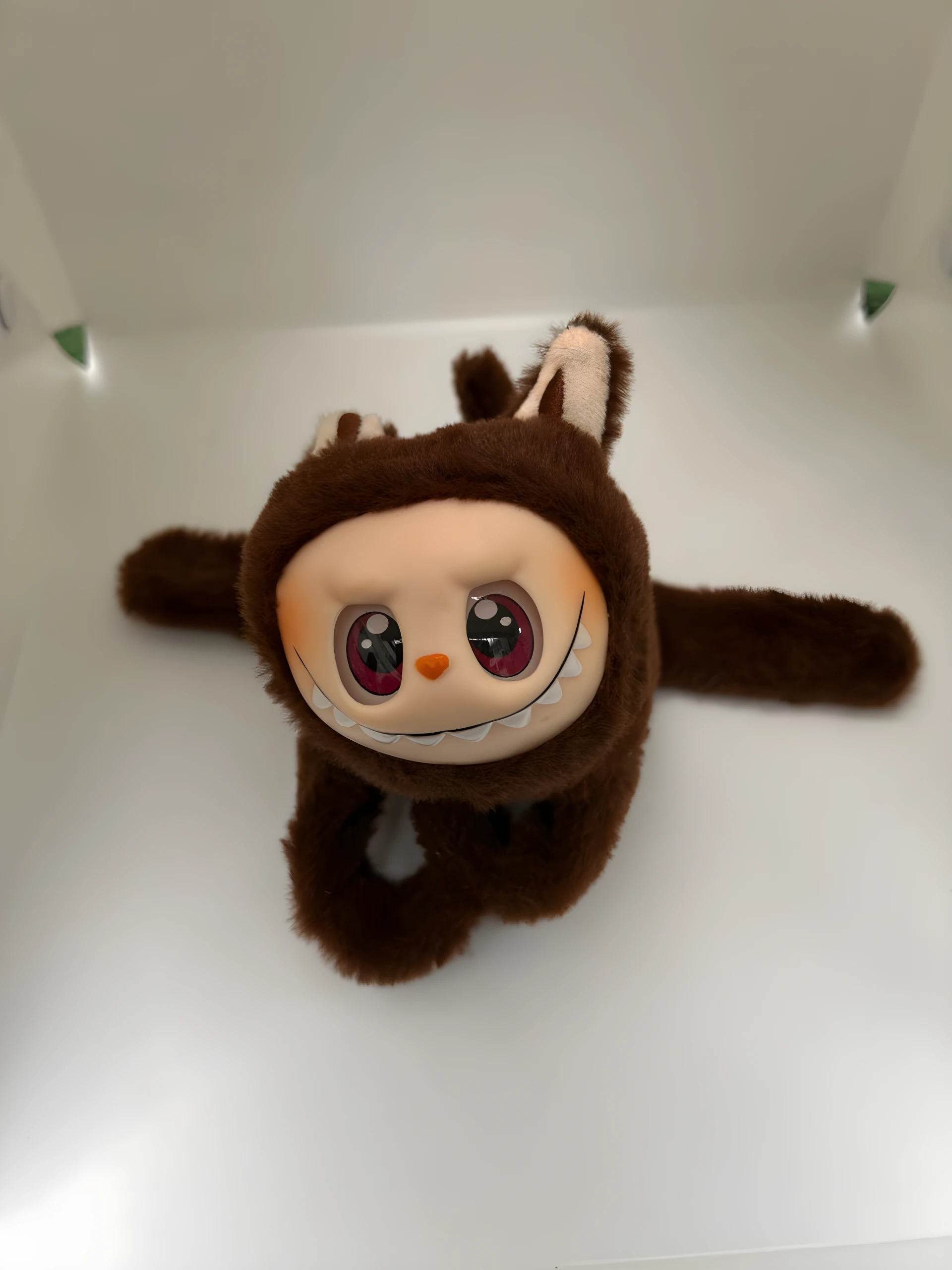 Peluche Labubu marrón peludo con orejas, rostro de vinilo blanco, ojos grandes morados brillantes y sonrisa con dientes puntiagudos, colgando sobre fondo blanco.