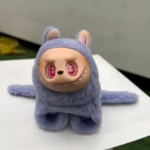 Peluche coleccionable Labubu lavanda, textura peluche, rostro blanco con ojos rosados de corazón y dientes puntiagudos.