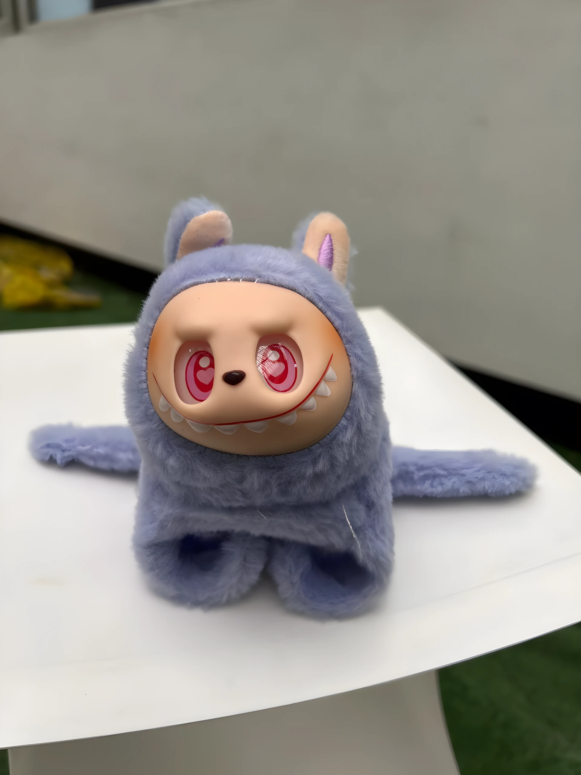 Peluche coleccionable Labubu lavanda, textura peluche, rostro blanco con ojos rosados de corazón y dientes puntiagudos.