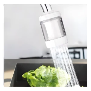 Mini purificador de agua para grifo blanco enjuagando lechuga fresca en un fregadero.