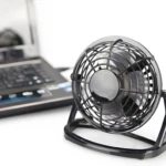Mini ventilador USB negro con base ajustable junto a laptop.