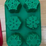 Molde de silicona verde con 6 cavidades de copos de nieve para repostería navideña.