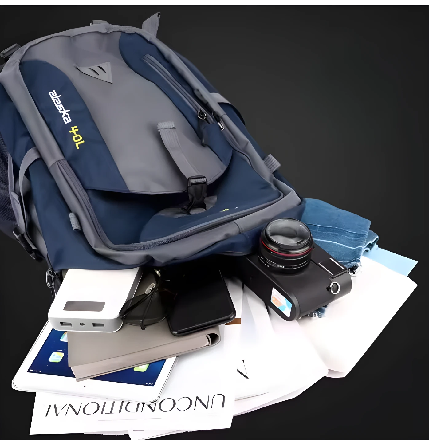 Morral de viaje azul y gris con cámara, tablet, celular y cargador portátil dentro.