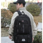 Mochilero negro para hombre, con logo plateado y correas ajustables, visto desde atrás.