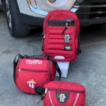 Morral Totto rojo acolchado con llavero temático, lonchera y cartuchera a juego, al frente de un vehículo.