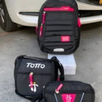 Set de morral, cartuchera y lonchera Totto negros con detalles fucsia, diseño infantil, expuestos sobre superficie de concreto.