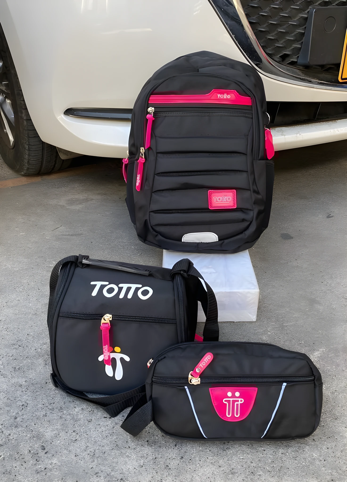 Set de morral, cartuchera y lonchera Totto negros con detalles fucsia, diseño infantil, expuestos sobre superficie de concreto.