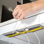 Organizador de cables adhesivo gris y amarillo en la parte inferior de un escritorio, sujetando cables y un adaptador USB.