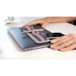 Organizador adhesivo gris con bandas moradas y rosas para sostener bolígrafo y celular en portátil.