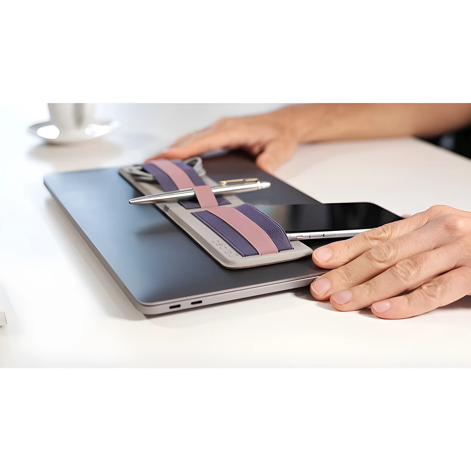 Organizador adhesivo gris con bandas moradas y rosas para sostener bolígrafo y celular en portátil.