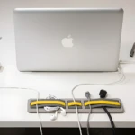 Organizador gris con bandas amarillas sujetando cables y audífonos junto a laptop Apple y smartphone.