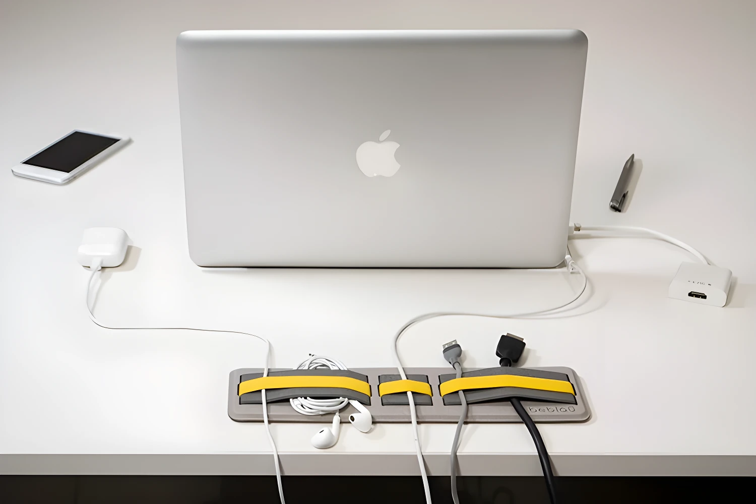 Organizador gris con bandas amarillas sujetando cables y audífonos junto a laptop Apple y smartphone.