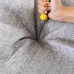 Contenedor de ropa 110L con tapa reforzada, mostrando la mano de una persona con un destornillador presionando la tela de patrón de espiga.