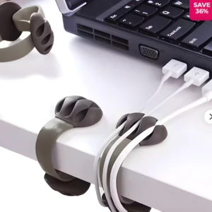 Dos clips sujetacables adhesivos grises organizan cables blancos junto al borde de un escritorio, cerca de un portátil.