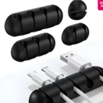 Organizadores adhesivos negros de silicona para cables. Se ven dos piezas de 4 ranuras y piezas sueltas, sujetando cables USB en un escritorio blanco.