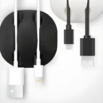 Organizador de cables negro y blanco sosteniendo cables USB-A, Lightning y USB-C en escritorio minimalista.