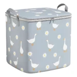 Canasta organizadora de ropa gris con tapa y cremallera, decorada con gansos blancos y margaritas, con asas grises.