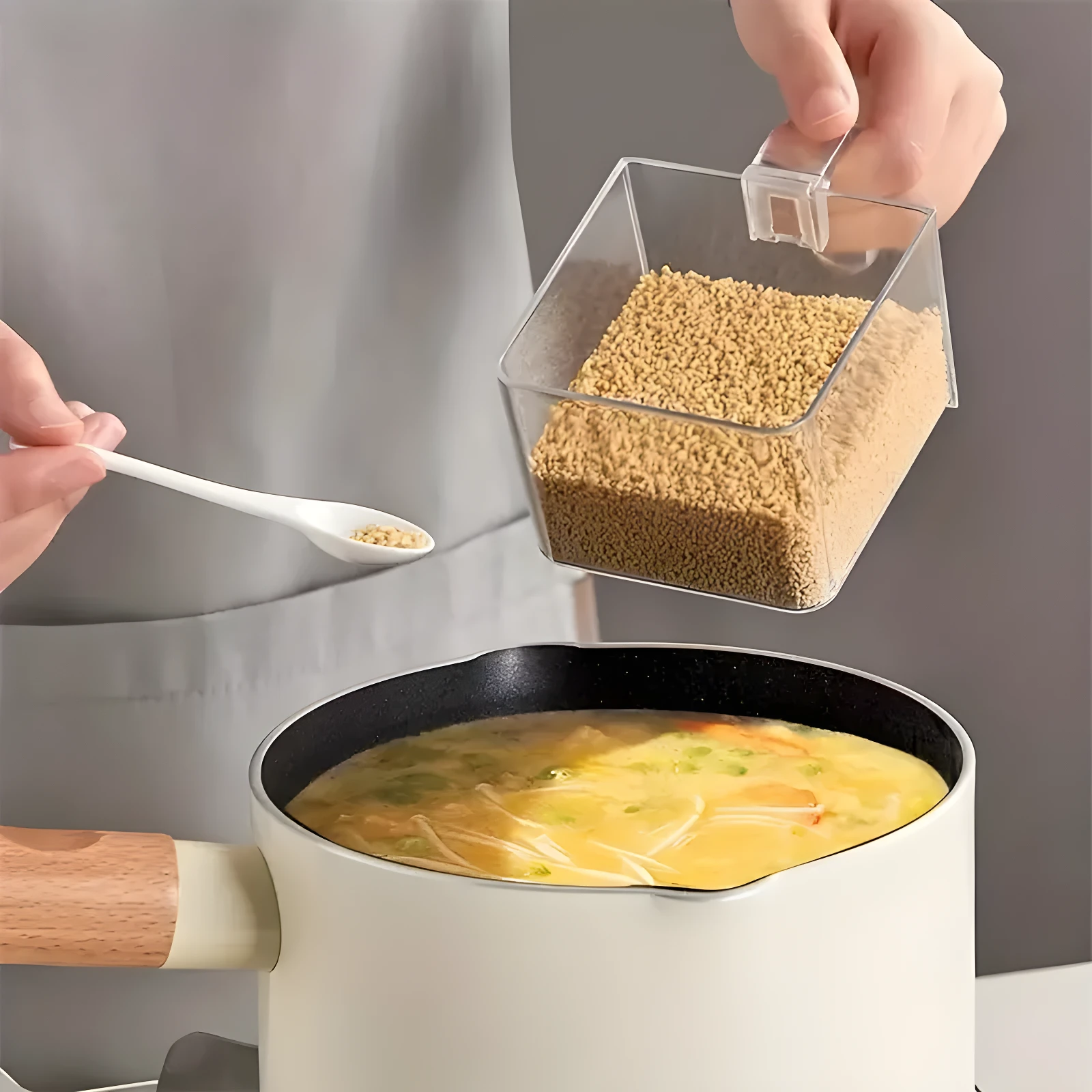 Recipiente transparente con clip para organizar especias, con cuchara sirviendo condimento a una olla con sopa.