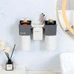 Organizador de pared gris y blanco para baño, sostiene dos vasos invertidos, perfume y aplicador, con espacio central para brochas.