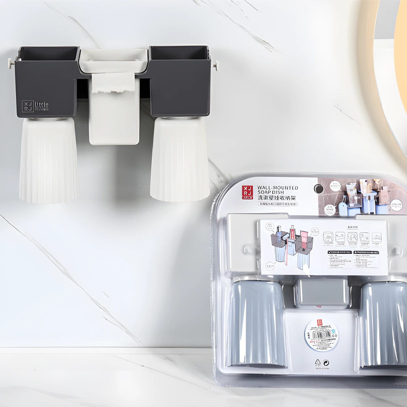 Organizador de baño montado en pared con dos compartimentos oscuros y vasos blancos invertidos. Empaque muestra variante gris y azul.