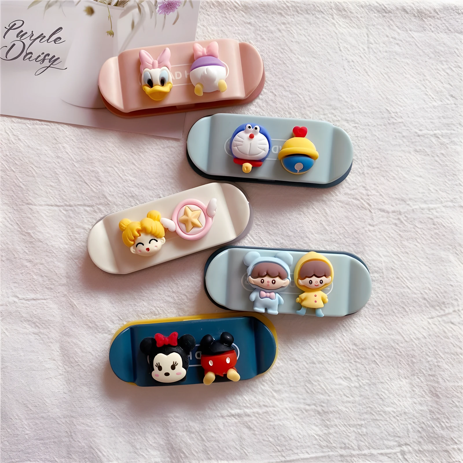 Cinco soportes organizadores de cable tipo patineta con figuras 3D: Daisy/Pato Donald, Doraemon, Sailor Moon, niños con capucha y Mickey/Minnie.