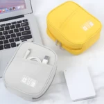 Dos estuches organizadores de cables, uno gris con USB visible y uno amarillo, junto a un disco duro blanco y un portátil.