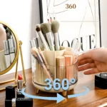 Organizador giratorio 360° de maquillaje acrílico ámbar con compartimentos, guarda brochas y labiales junto a espejo dorado.