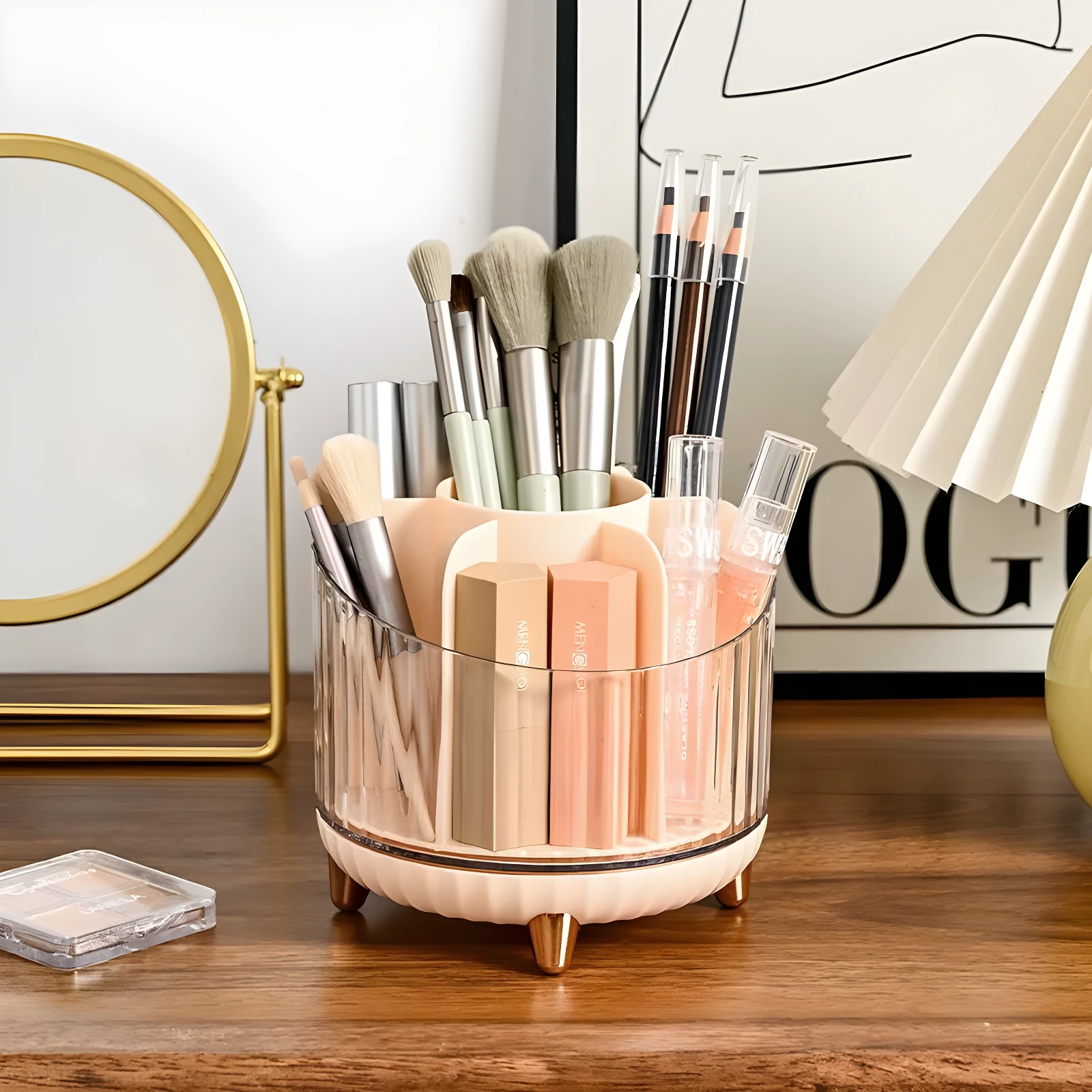Organizador de maquillaje giratorio transparente con base beige y patas doradas, exhibiendo brochas, labiales y lápices de ojos sobre una cómoda de madera.