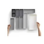 Organizador de cubiertos gris y blanco, varias secciones, manos acomodando las piezas.