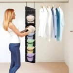 Organizador colgante negro para gorras, con 8 compartimentos, en clóset con camisas.