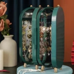 Organizador de joyas verde con patas doradas, dos puertas abatibles y varios compartimentos para exhibir collares y aretes.
