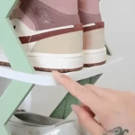 Zapatillas deportivas color rosa y beige sobre organizador de zapatos multiestante verde y blanco.