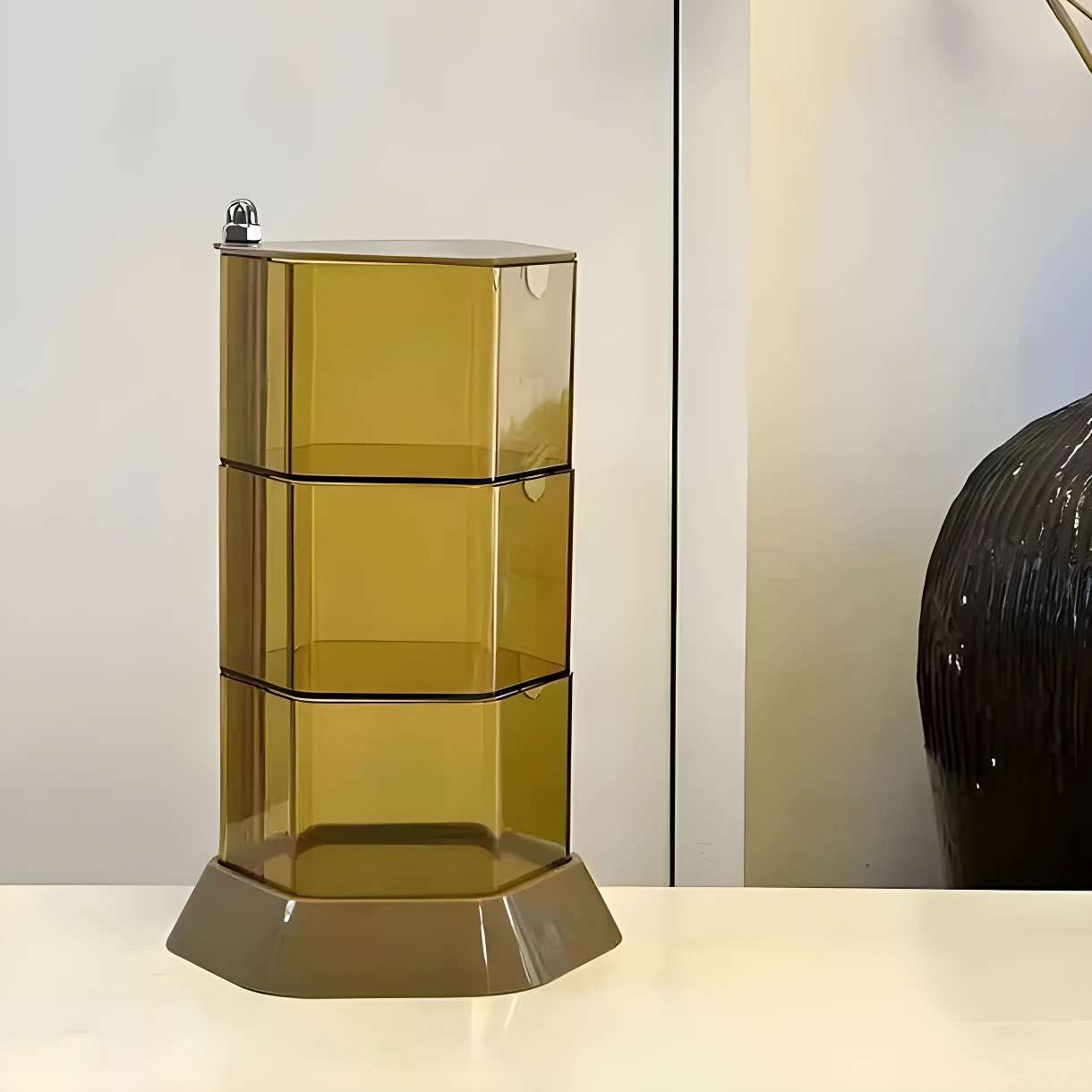 Organizador giratorio de 3 niveles en tono ámbar translúcido, con base gris oscuro, para joyas y cosméticos.