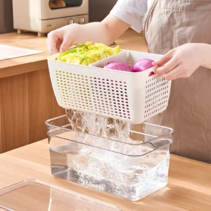 Canasta escurridora blanca con lechuga y cebollas rojas drenando agua hacia un contenedor transparente inferior.