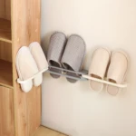 Zapateros organizadores adhesivos con tres pares de pantuflas rayadas (beige y gris) colgados a la pared y un par al costado de un mueble de madera.