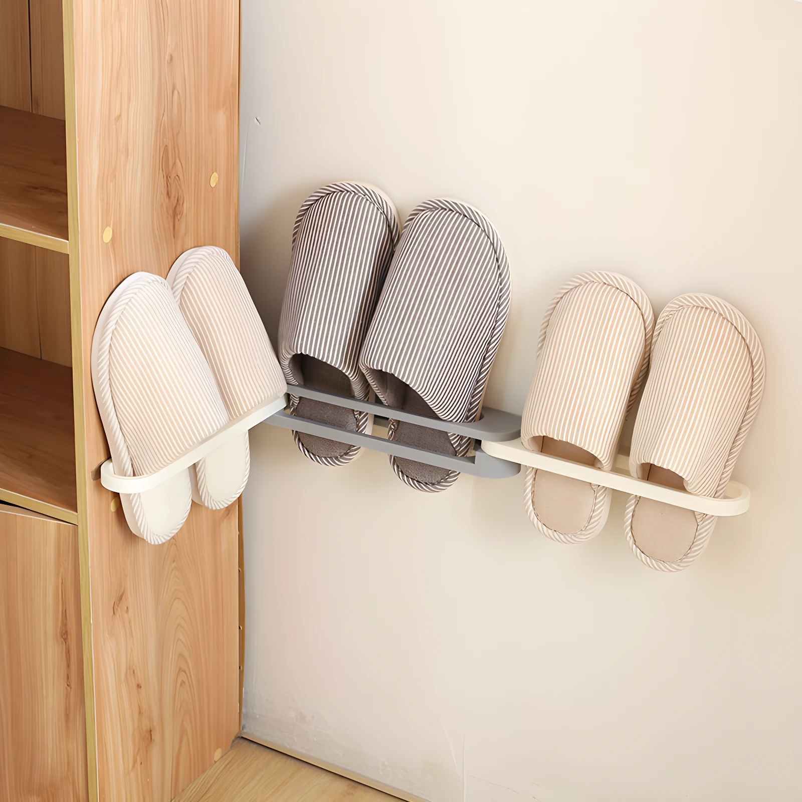 Zapateros organizadores adhesivos con tres pares de pantuflas rayadas (beige y gris) colgados a la pared y un par al costado de un mueble de madera.