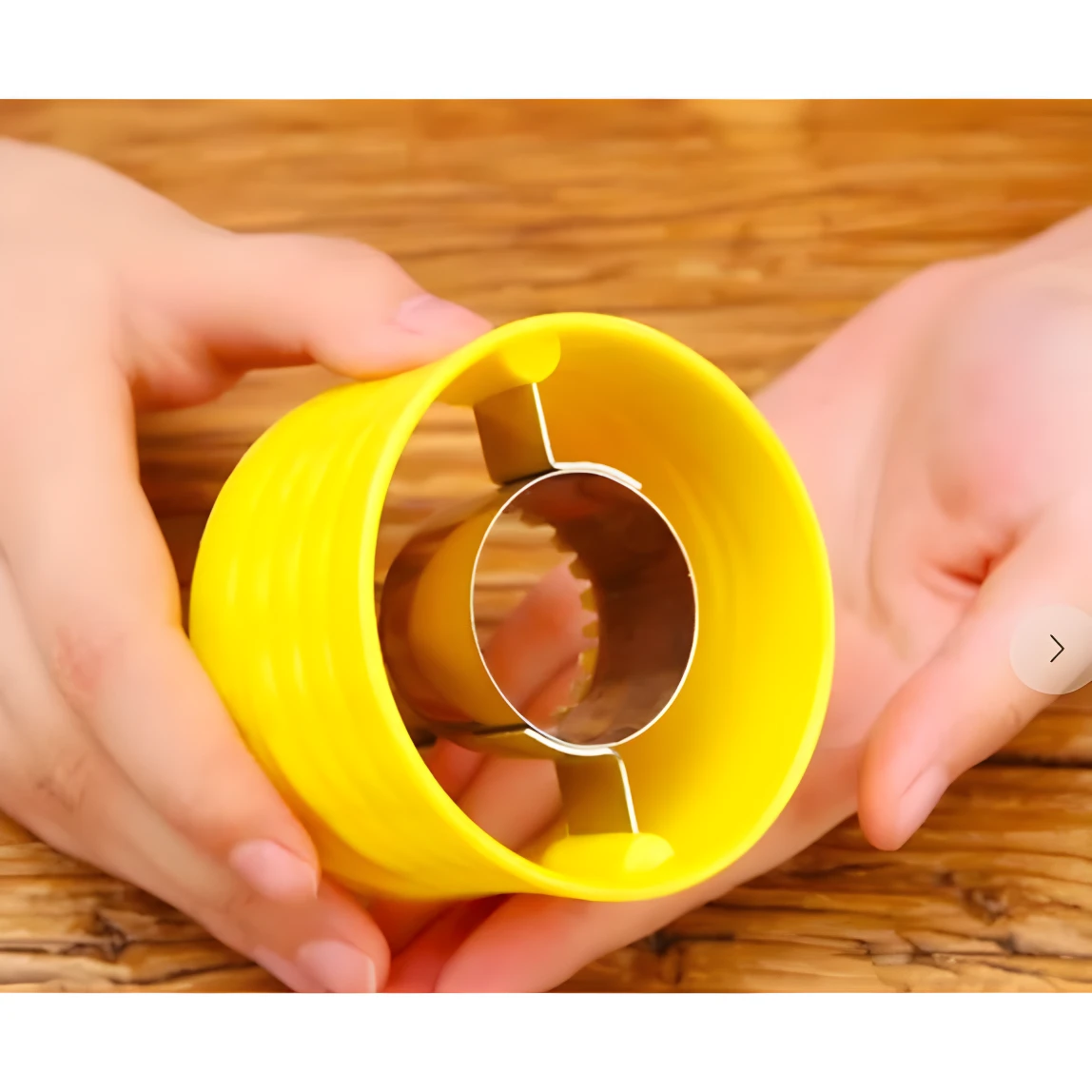 Manos sostienen pelador desgranador de maíz amarillo con inserto metálico dentado, fondo madera.