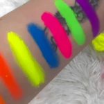 Pigmentos en polvo neón para nail art y maquillaje profesional, aplicados en mano en tonos naranja, amarillo, azul, fucsia, verde y morado.